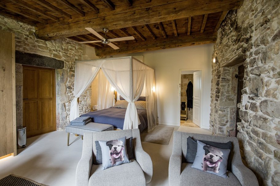 Suite avec lit à baldaquin drapé de voiles blancs, murs en pierre et poutres en chêne anciens